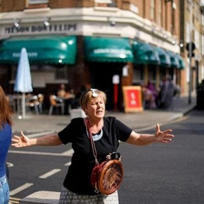 A person standing on a crossing on a city street with arms outstretched talking