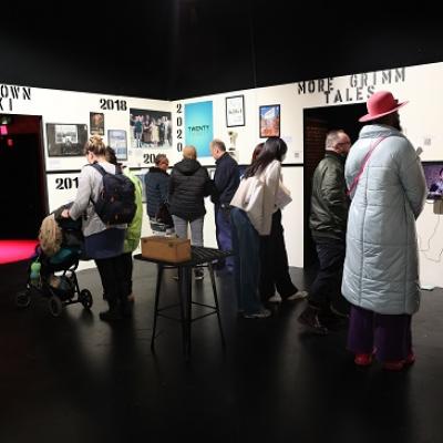 A group of people walking around a room looking at a large immersive Taking Part Young Vic timeline