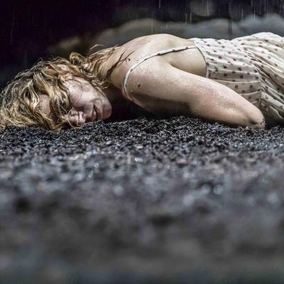 Billie Piper (Her) lies on her side, cold at wet on the mud in Yerma at the Young Vic by Johan Persson