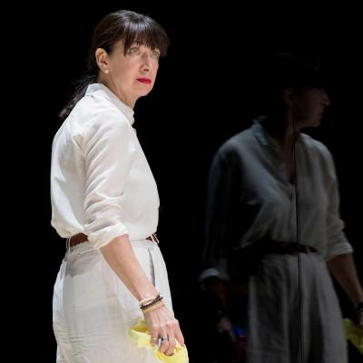 Maureen Beattie stands with a yellow cleaning cloth, reflected in the glass in Yerma at the Young Vic by Johan Persson