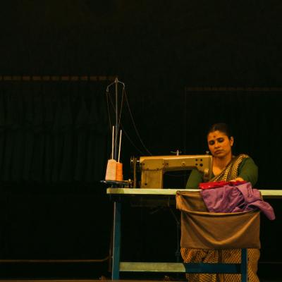 Zainab Hasan sitting at sewing machine, working on a garment. Isha Shah.