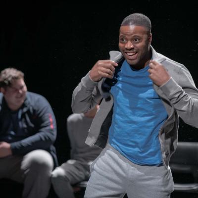 A grinning male performer adjusts the collar his hoodie, beaming out to the audience © Leon Puplett
