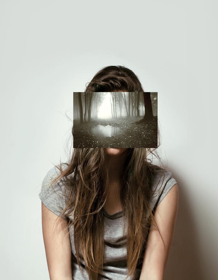 Female in front of a plain grey backdrop with her face concealed by an image of a misty forest