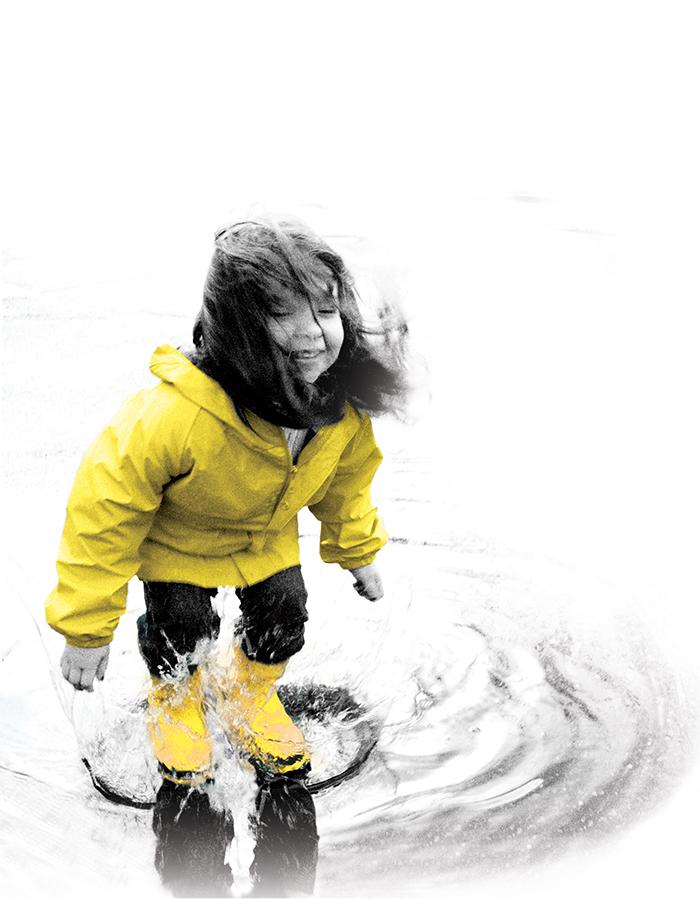 Little girl in a yellow jacket plays in a puddle