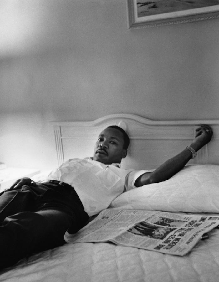 black and white image of dr martin luther king laying on a bed with newspapers beside him