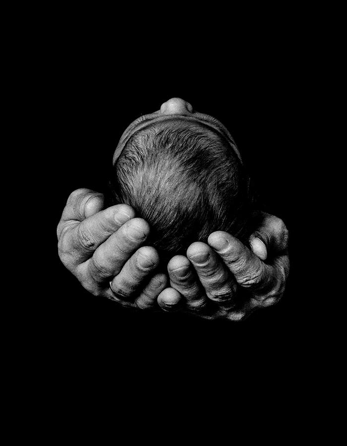 black and white image of two hands holding a babies head