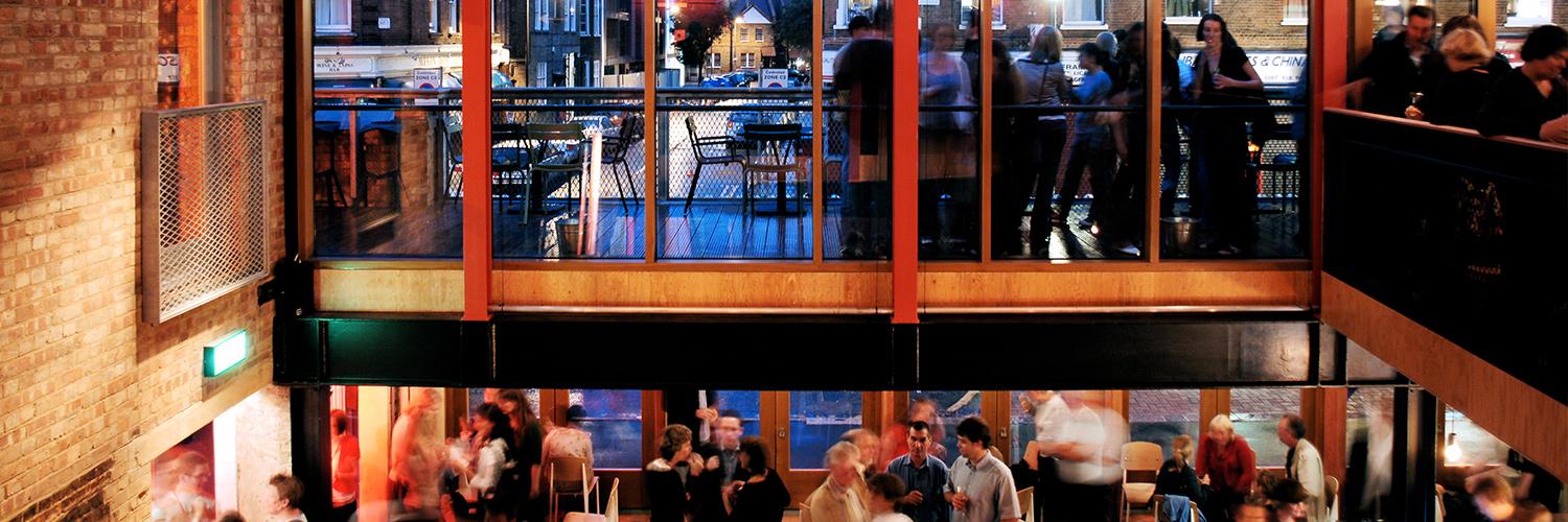 A photo taken at dusk, looking from the top of the stairs across to the windows looking out onto The Cut from inside The Cut Bar.