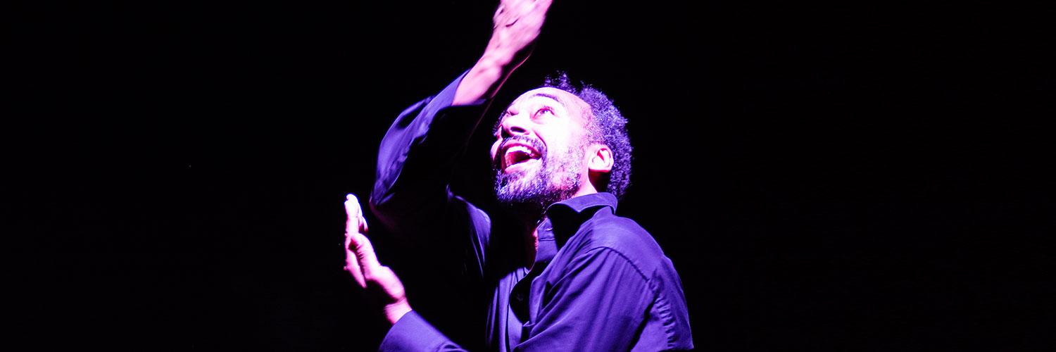 Man in a darkly lit atmosphere, arms stretched, looking upwards