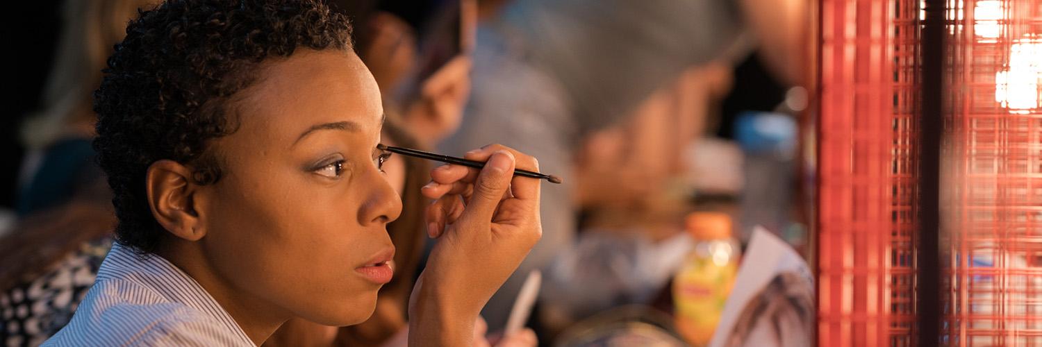 a person doing their makeup in front of a lit mirror