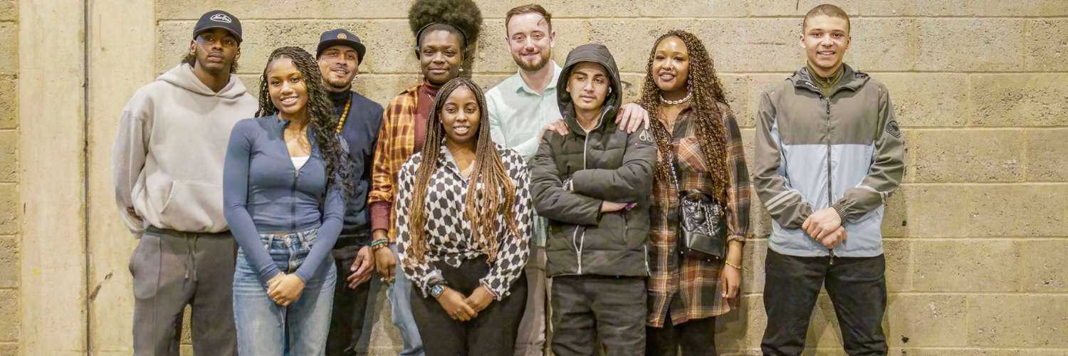 A group of people stood smiling against a gray wall