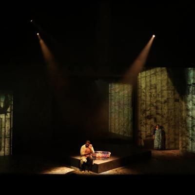 Irfan Shamji sitting holding a baby and Zainab Hasan standing to the side. Projections on the walls show birds and leaves. Akhila Krishnan.