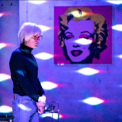 Paul Bettany in The Collaboration (c) Marc Brenner. Warhol, bathed in purple and glitterball light with a Marilyn Monroe in the background