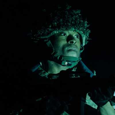 A soldiers face can be seen looking into the distance. The image is very dark and the light is just picking out his face and helmet. 