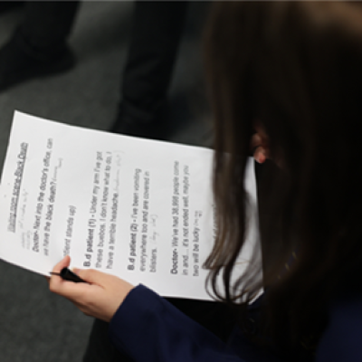 The back of a student’s head looking at a script for roleplaying a medieval waiting room scene. 