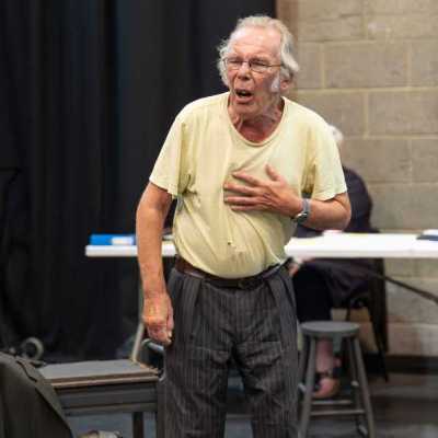 An older man performs a scene in a theatre rehearsal room
