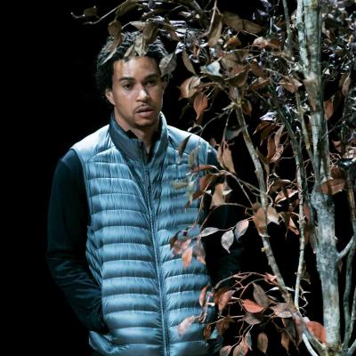 John McMillian (Victor) stands half obscured by a dying tree in Yerma at the Young Vic. Photo by Johan Persson