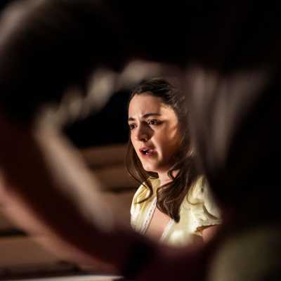A woman light yellow dress sitting on the bed.