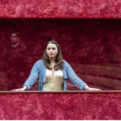 A woman in yellow dress and blue cardigan standing behind a displaying window	