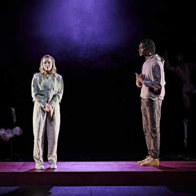 Two people stand in a spotlight speaking 