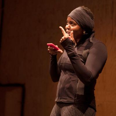 A woman dressed in running gear, talking on a phone on loudspeaker.