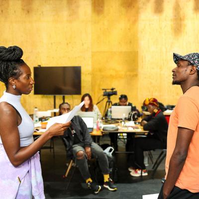 Actress Danielle Kassaraté and Actor John Rwothomach face eachother and stare. Members of the Taking Part team sit watching their performance.