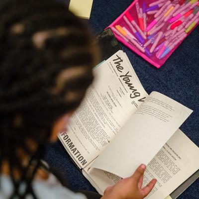 Shot taken from over someone's shoulder, showing a person looking through a file of documents from the Young Vic archive