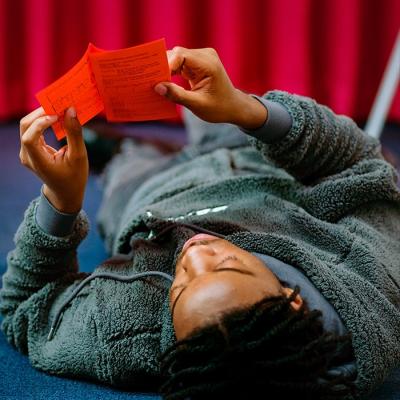 A person lying on the floor, holding a pamphlet over their head to read it