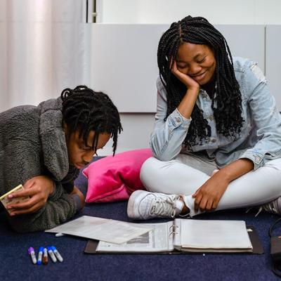 Two people looking at some pieces of paper on the floor, with one person lying on the floor and one person sitting cross-legged