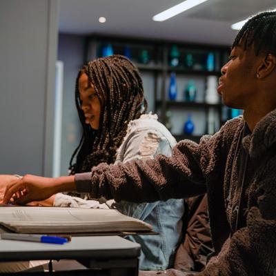 Two people sitting at a table, looking at pieces of paper and talking to each other