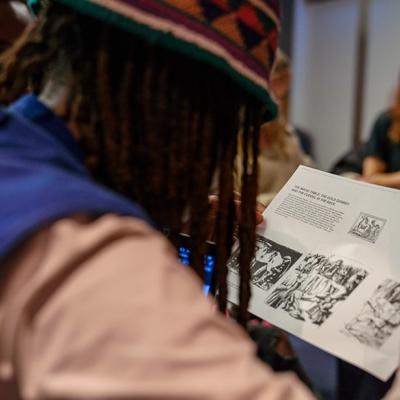 A shot over a person's shoulder as they look at a piece of paper with multiple illustrations and some text on it, including a headline: 'The Magic Table, The Gold Donkey, and the Cudgel in the Sack'