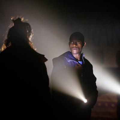 John Pfumojena (Okot) lit by torchlight in The Jungle at the Young Vic © David Sandison