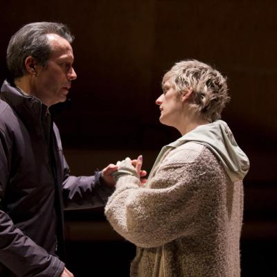 Jonathan Cullen (Man) is standing on the left of the photo wearing a dark jacket with Maisie Greenwood (Woman) in a light jacket holding his oustretched hand. Winter at the Young Vic © Ellie Kurttz