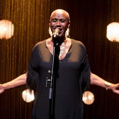 Josette Bushell-Mingo in Nina with beautiful fringed curtains and show lights behind her. Photo by Simon Annand