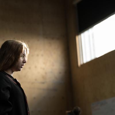 A young female actor is staring off into the distance as she stands on the left of frame, lit by natural light through a window above her © Leon Puplett