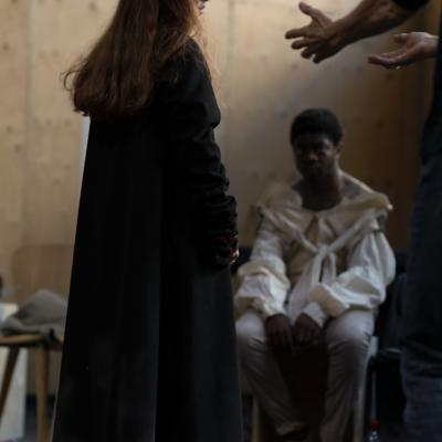 A pair of hands are held out from an unseen actor towards the young woman in the centre of the shot who looks back, seemingly frightened © Leon Puplett