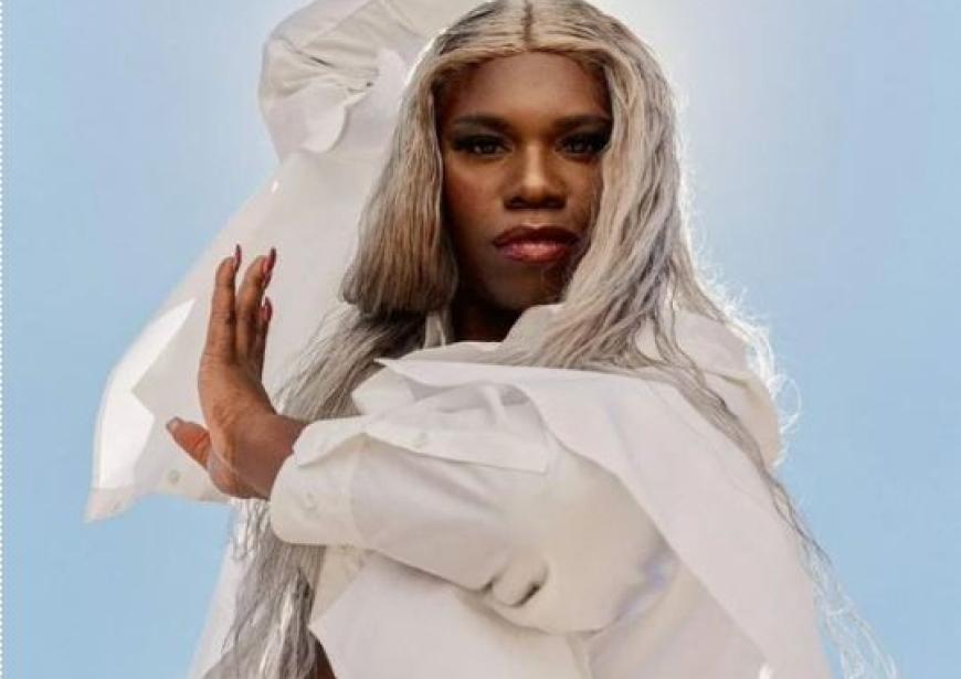A person, in a white cloak, with one arm above their head and the other across their chest