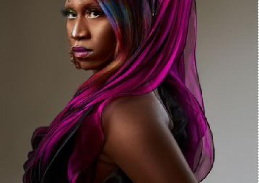 A person with purple long hair, looking over their shoulder