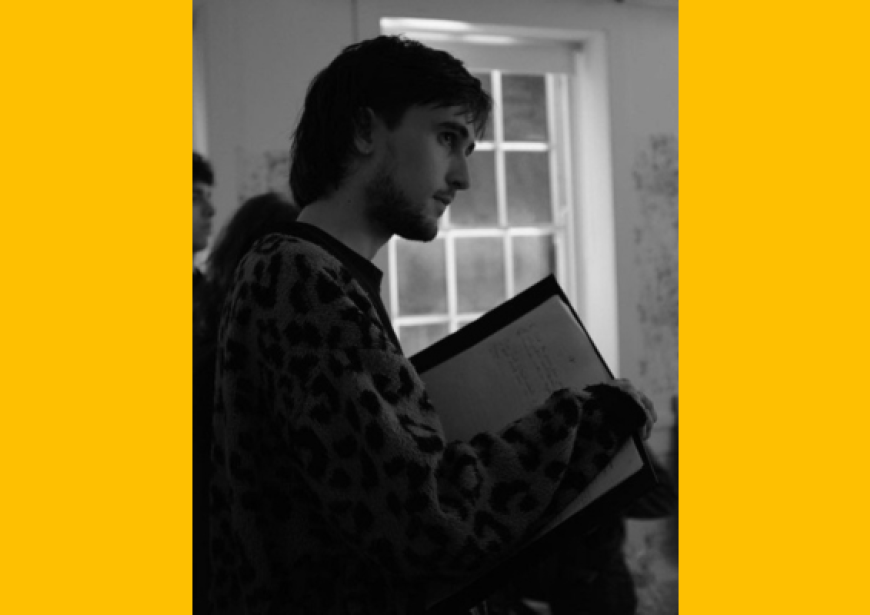 The side of a person wearing a jumper and holding a script.