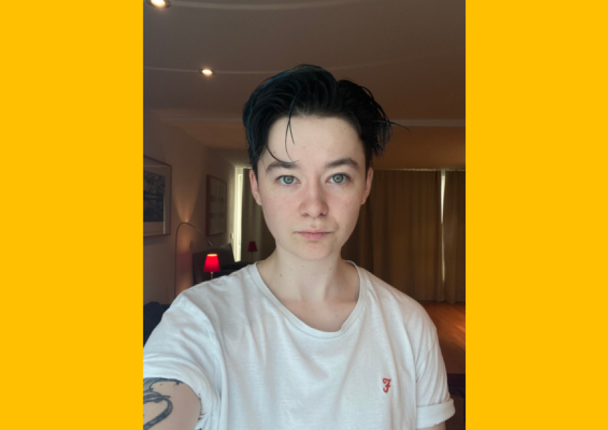 A headshot of a person with short dark hair wearing a white t-shirt.