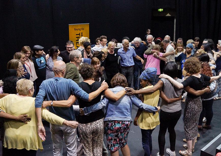 People standing in a circle in a workshop with their arms around each other.