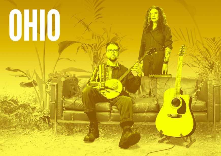 Against a yellow background are a man and woman. The man sits on a sofa and is holding a banjo; the woman stands behind the sofa. Next to them is a guitar on a stand.