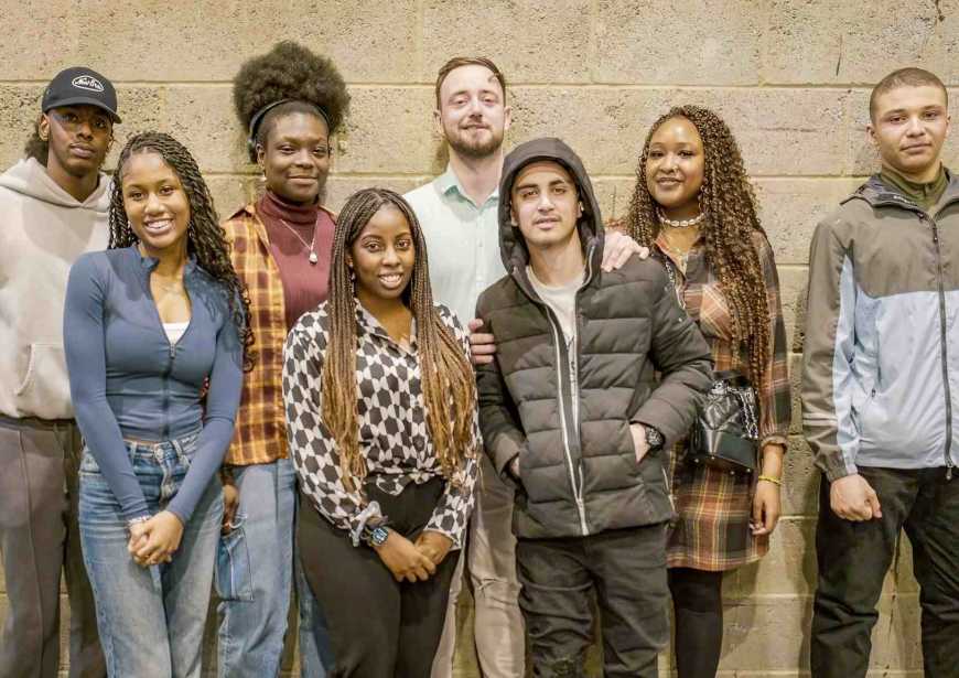 A group of people stood smiling against a gray wall