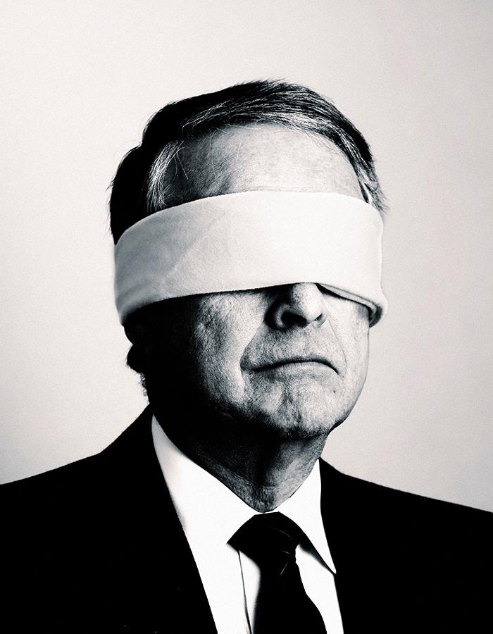 A man in a suite, with black tie, blindfolded