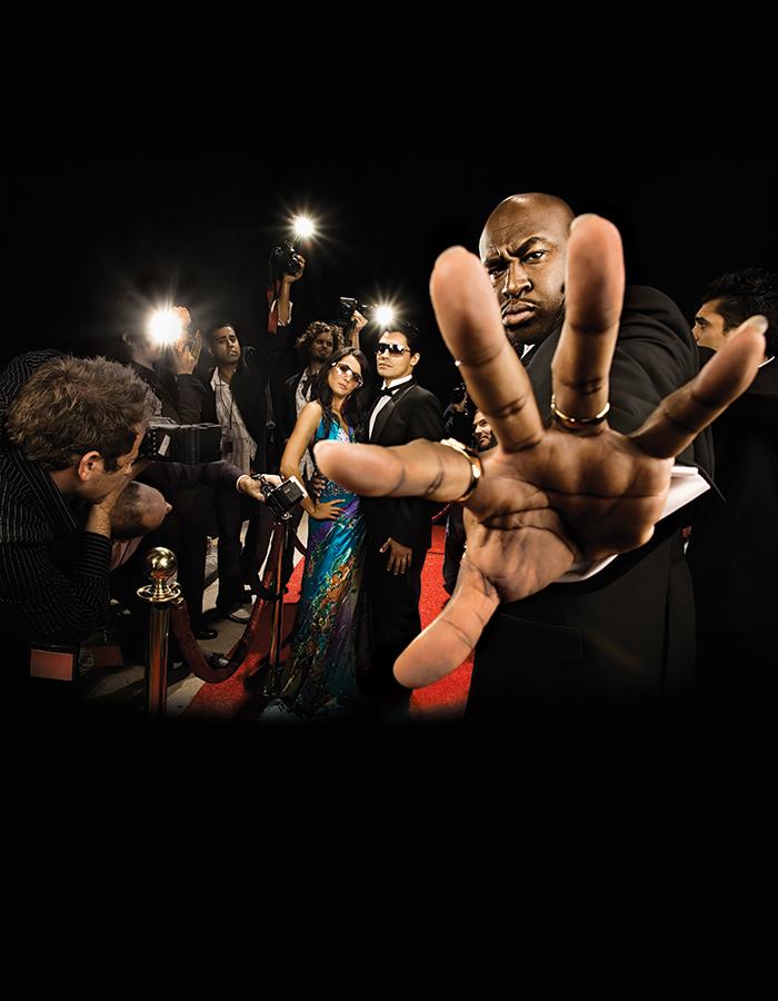 Orpheus on a red carpet being photographed by Paparazzi, hand outstretched to block camera
