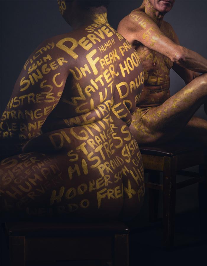 A naked male and female body both with negative and positive words such as freak, daughter, hooker, human, painted in gold