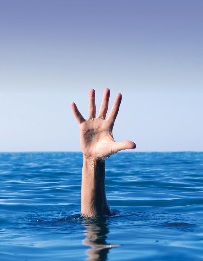 A hand comes out of the sea, reaching for help against a blue sky 