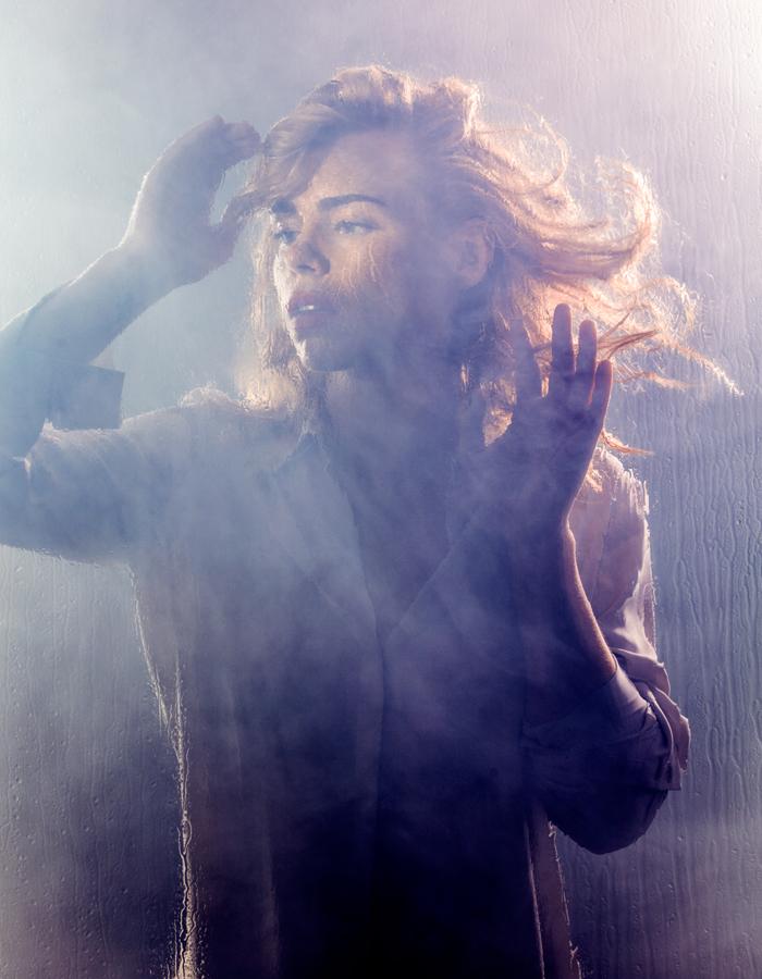 Billie Piper stands behind a misty pane of glass looking wistfully into the distance