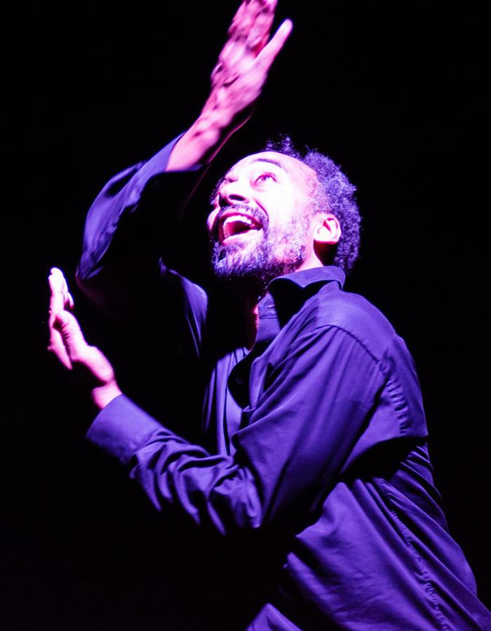 Man in a darkly lit atmosphere, arms stretched, looking upwards
