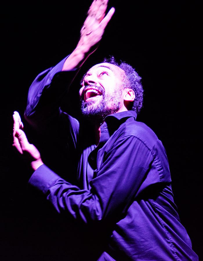 Man in a darkly lit atmosphere, arms stretched, looking upwards