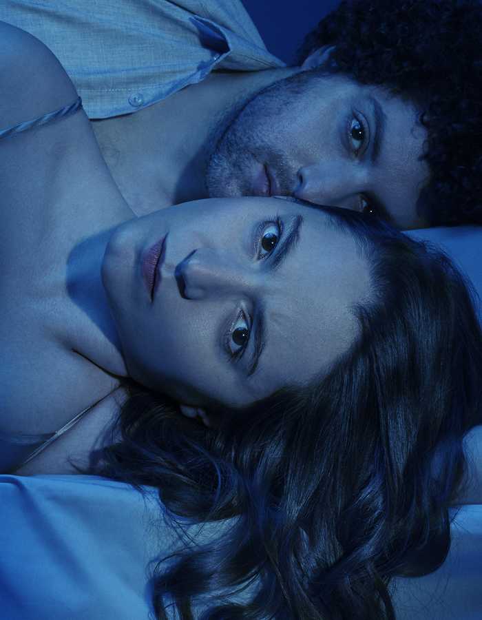 A man and a woman lie on a bed with light sheets. They both stare straight into the camera, awash in blue light. over the image, there is white text reading: Arthur Miller/Broken Glass/directed by Jordan Fein
